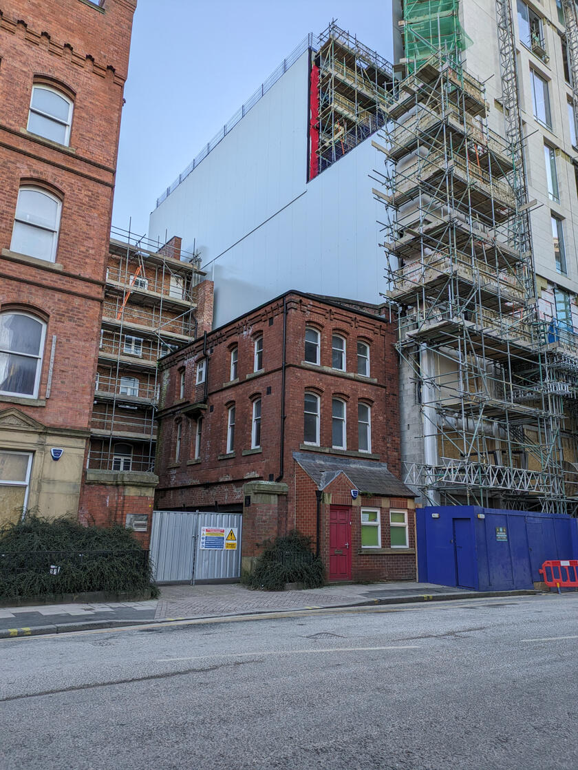 Small, old building cowering next to a larger new building, Leeds